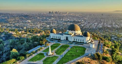 Aerial view of the Griffith Observatory with downtown Los Angeles in the background, bathed in golden sunlight.