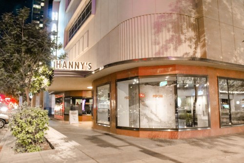 Exterior of Hanny's restaurant at night, featuring large windows and a modern design, with city lights in the background.