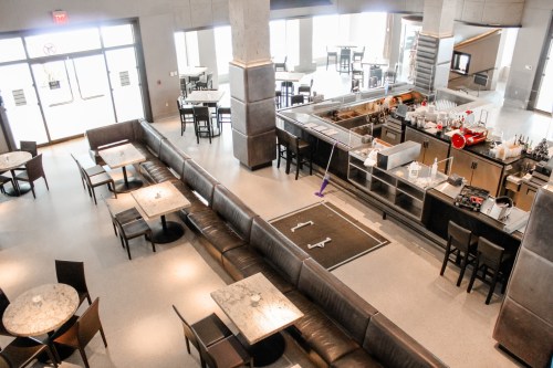 A spacious restaurant interior featuring tables, a bar area, and large windows, with modern decor and seating.