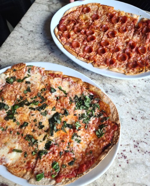 Two pizzas on white plates: one with cheese and herbs, the other topped with pepperoni, on a marble table.
