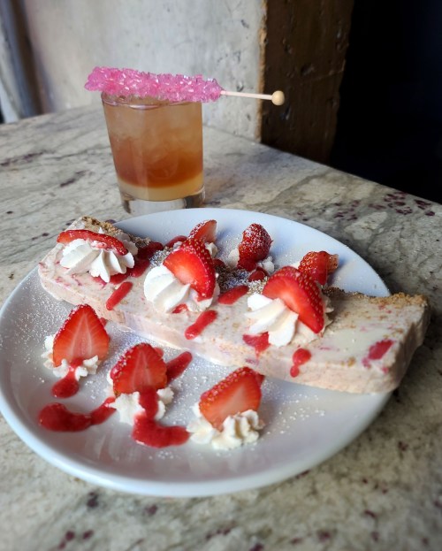 A dessert plate with strawberry ice cream, whipped cream, and strawberry sauce, alongside a colorful drink with a garnish.