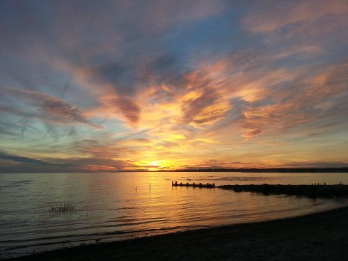 A serene sunset over a calm lake, with colorful clouds reflecting on the water and a silhouette of a pier in the distance.