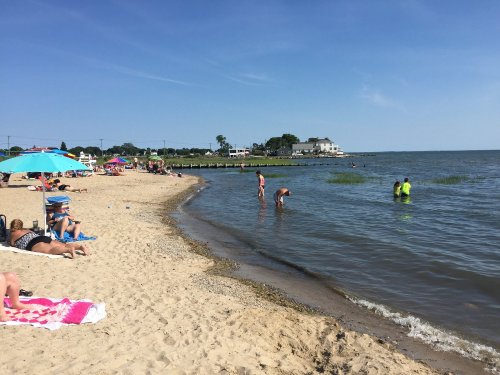 A sunny beach scene with people relaxing on the sand, swimming, and colorful umbrellas lining the shore.