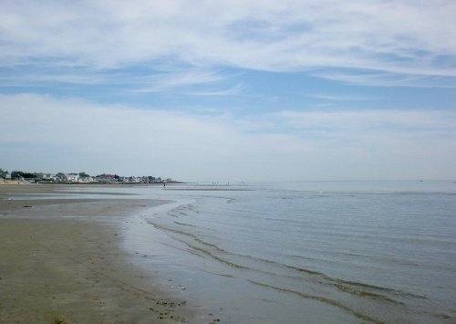 A serene beach scene with gentle waves, a cloudy sky, and distant shoreline.