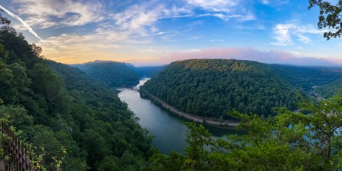 A panoramic view of a river winding through lush green hills under a colorful sky at sunset.