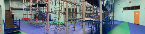 Indoor playground featuring climbing structures, nets, and slides on colorful flooring.