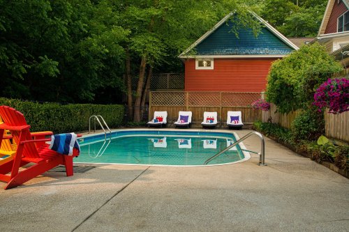 A serene backyard pool area with red chairs, colorful towels, and lush greenery surrounding the inviting water.