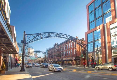 A city street with an archway, historic buildings, modern architecture, and cars driving under a clear blue sky.