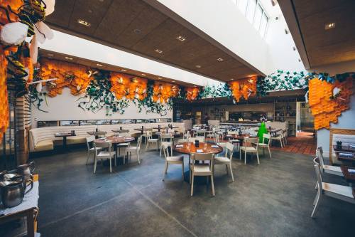 Bright, modern restaurant interior with wooden tables, white chairs, and vibrant orange wall decor featuring greenery.