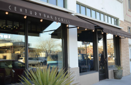 Exterior of Century Bar & Grill featuring large windows and a canopy sign, with potted plants at the entrance.