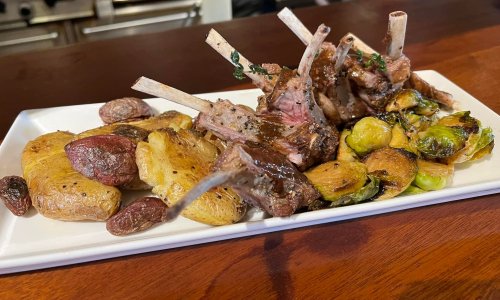 A plate of lamb chops with roasted potatoes and Brussels sprouts, garnished with herbs.