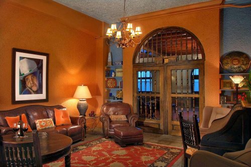 Cozy living room with leather furniture, warm orange walls, a chandelier, and a large framed portrait.
