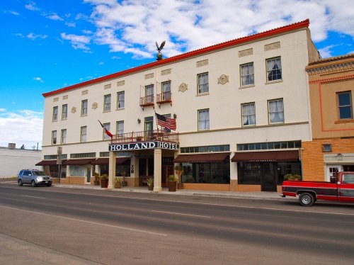 Historic Holland Hotel with a white facade, flags, and a red truck parked in front, set against a blue sky.