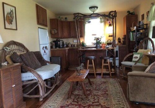 Cozy living room with wooden furniture, a mirror, and a rug, featuring a kitchen area in the background.