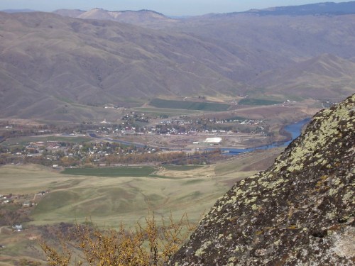 A panoramic view of rolling hills and a river, with a small town nestled in the valley below.