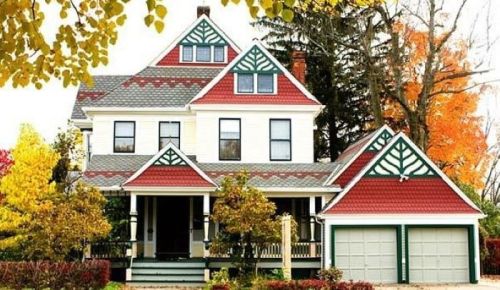 A charming Victorian-style house with a red and green roof, surrounded by colorful autumn trees.