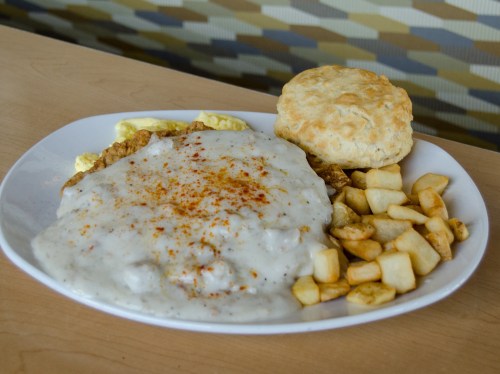 A plate of chicken fried steak topped with gravy, served with diced potatoes and a biscuit on the side.