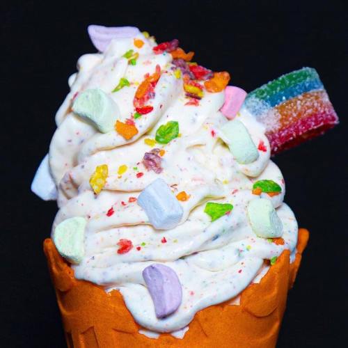 A colorful ice cream cone topped with swirls of creamy ice cream and various candies, set against a dark background.
