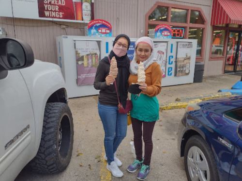 Two women holding large ice cream cones outside a shop, smiling and wearing casual clothing.