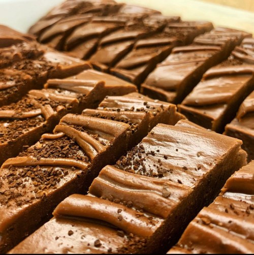Close-up of rich chocolate fudge, cut into squares, topped with chocolate shavings and a smooth, glossy finish.