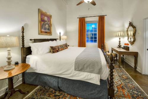 Cozy bedroom with a large bed, decorative pillows, warm lighting, and a window with orange curtains.