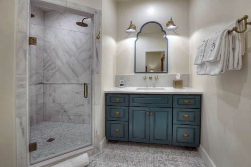 Modern bathroom featuring a glass shower, marble walls, a blue vanity, and elegant lighting.