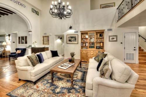 Cozy living room with two sofas, a coffee table, and a chandelier, featuring warm wood floors and decorative shelves.