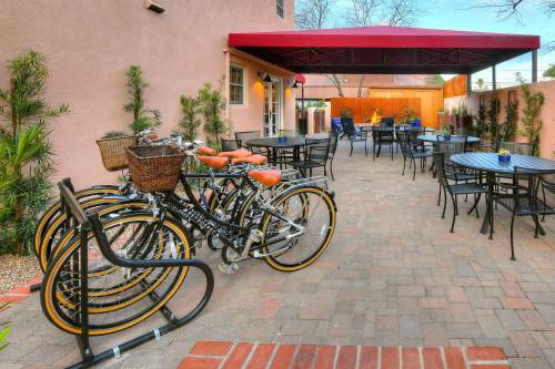 A cozy outdoor patio with bicycles parked, tables, and chairs under a red canopy surrounded by greenery.