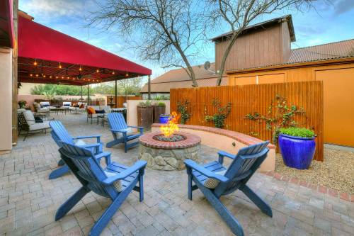 Cozy outdoor patio with blue chairs around a fire pit, surrounded by plants and a shaded seating area.