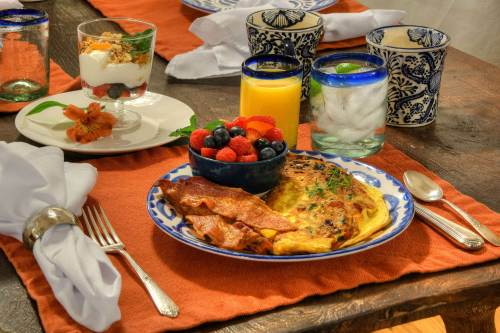 A beautifully set breakfast table featuring an omelet, bacon, fruit, yogurt parfait, and drinks on a rustic table.