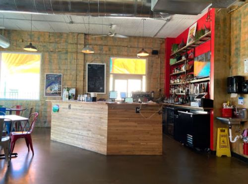A cozy café interior featuring a wooden counter, colorful walls, and seating with large windows letting in natural light.