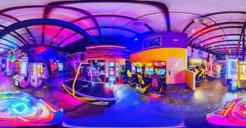 A vibrant arcade filled with colorful games and neon lights, featuring various arcade machines and a ping pong table.