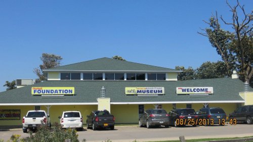 A yellow building with signs for a foundation and maritime museum, surrounded by parked cars under a clear blue sky.