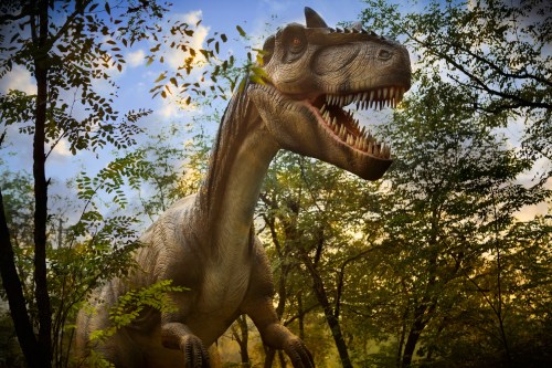 A large dinosaur with sharp teeth stands among trees in a prehistoric landscape under a colorful sky.