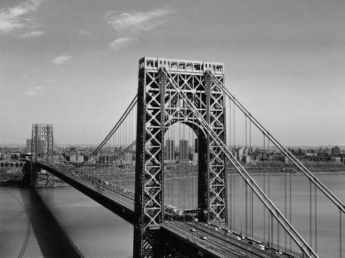 Black and white image of the George Washington Bridge spanning a river, with city skyline in the background.