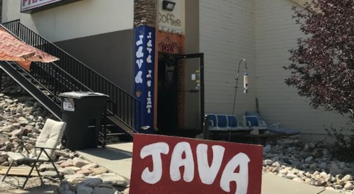 A coffee shop entrance with a large "JAVA" sign, surrounded by rocks and outdoor seating.