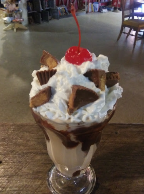 A tall glass dessert topped with whipped cream, chocolate sauce, peanut butter cups, and a cherry.