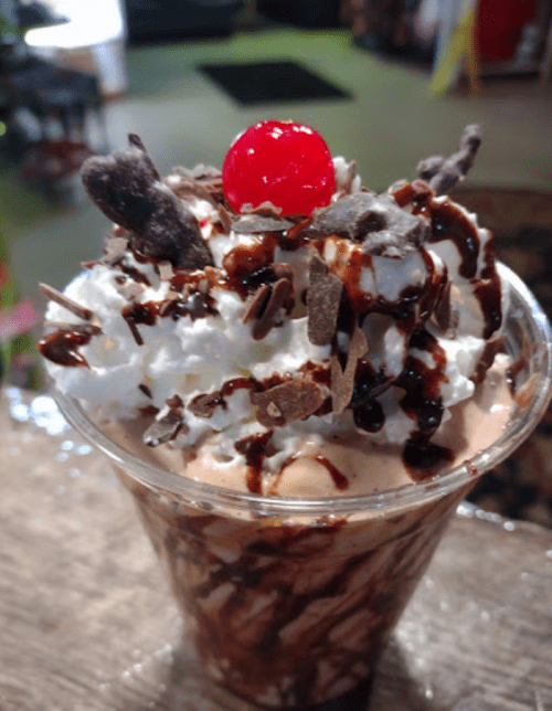 A delicious dessert in a cup topped with whipped cream, chocolate shavings, and a cherry.