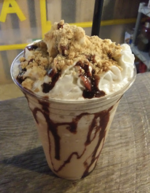 A creamy dessert drink topped with whipped cream, crushed cookies, and chocolate syrup in a clear cup.