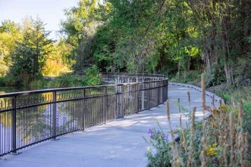 A winding pathway beside a calm waterway, surrounded by lush greenery and trees.