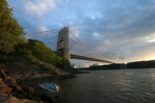 The George Washington Bridge spans the Hudson River, surrounded by lush greenery and a cloudy sky.