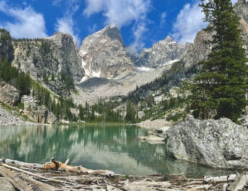 A serene mountain lake surrounded by towering peaks and lush greenery under a blue sky with scattered clouds.