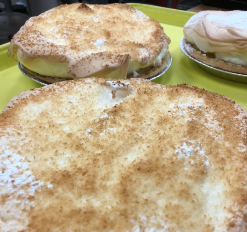 Two coconut cream pies with golden toasted meringue on a bright yellow tray.