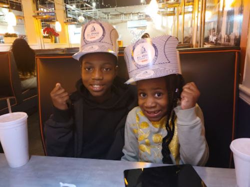 Two children wearing striped hats, smiling and posing at a diner table with drinks in front of them.