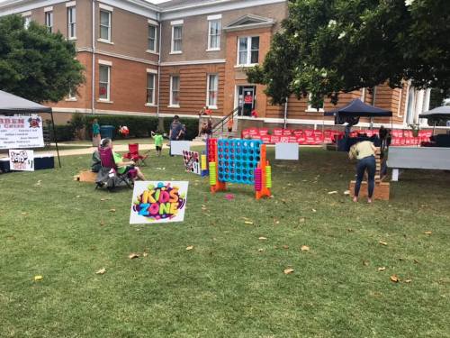 A community event with a "Kids Zone" sign, games, tents, and families enjoying activities on a grassy area.