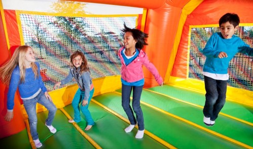 Four children joyfully jumping in a colorful bounce house, surrounded by netting and bright colors.