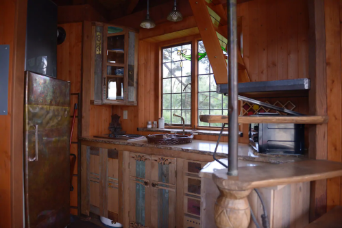 Cozy wooden kitchen with rustic cabinets, a large window, and various kitchen appliances.