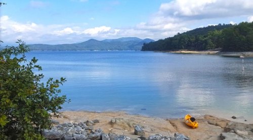 A serene lake scene with mountains in the background, a rocky shore, and a single yellow kayak on the water.
