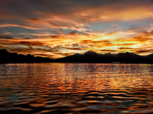 A vibrant sunset over a lake, with colorful clouds reflecting on the water and mountains in the background.