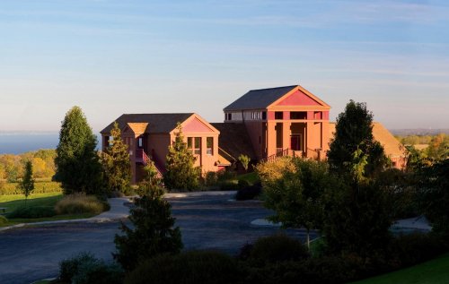 Two colorful houses surrounded by trees, with a scenic view of water and a clear sky in the background.